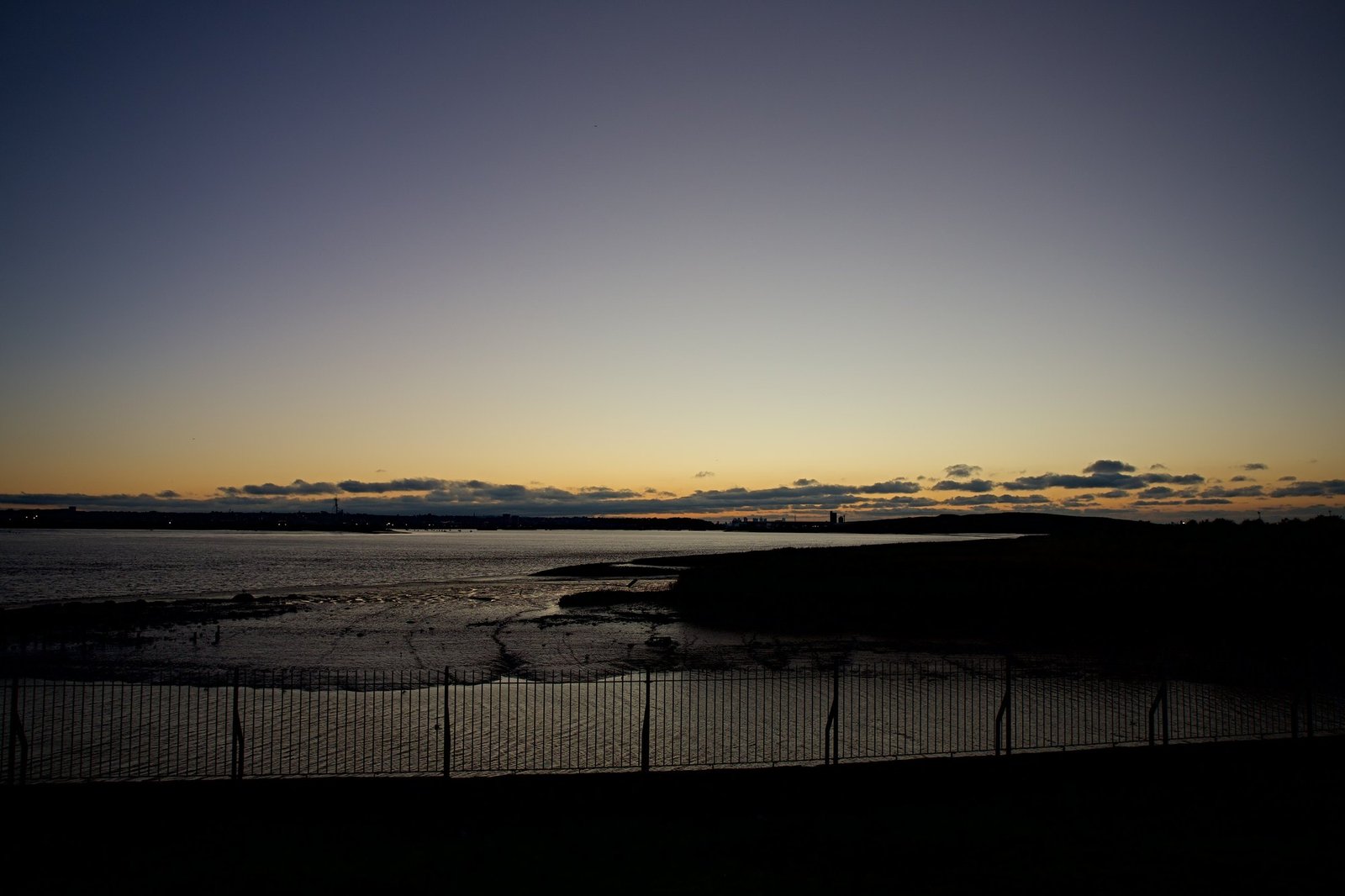Mudflats and channels at low tide under a fading orange horizon