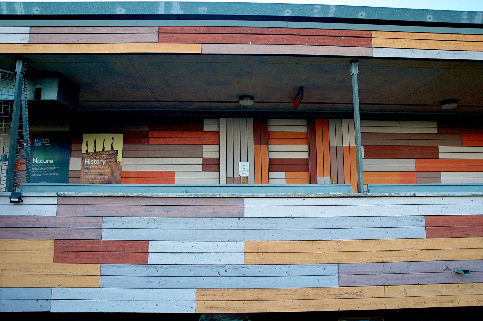 A head-on view of a veranda clad in painted timber boards of orange, red, grey and cream
