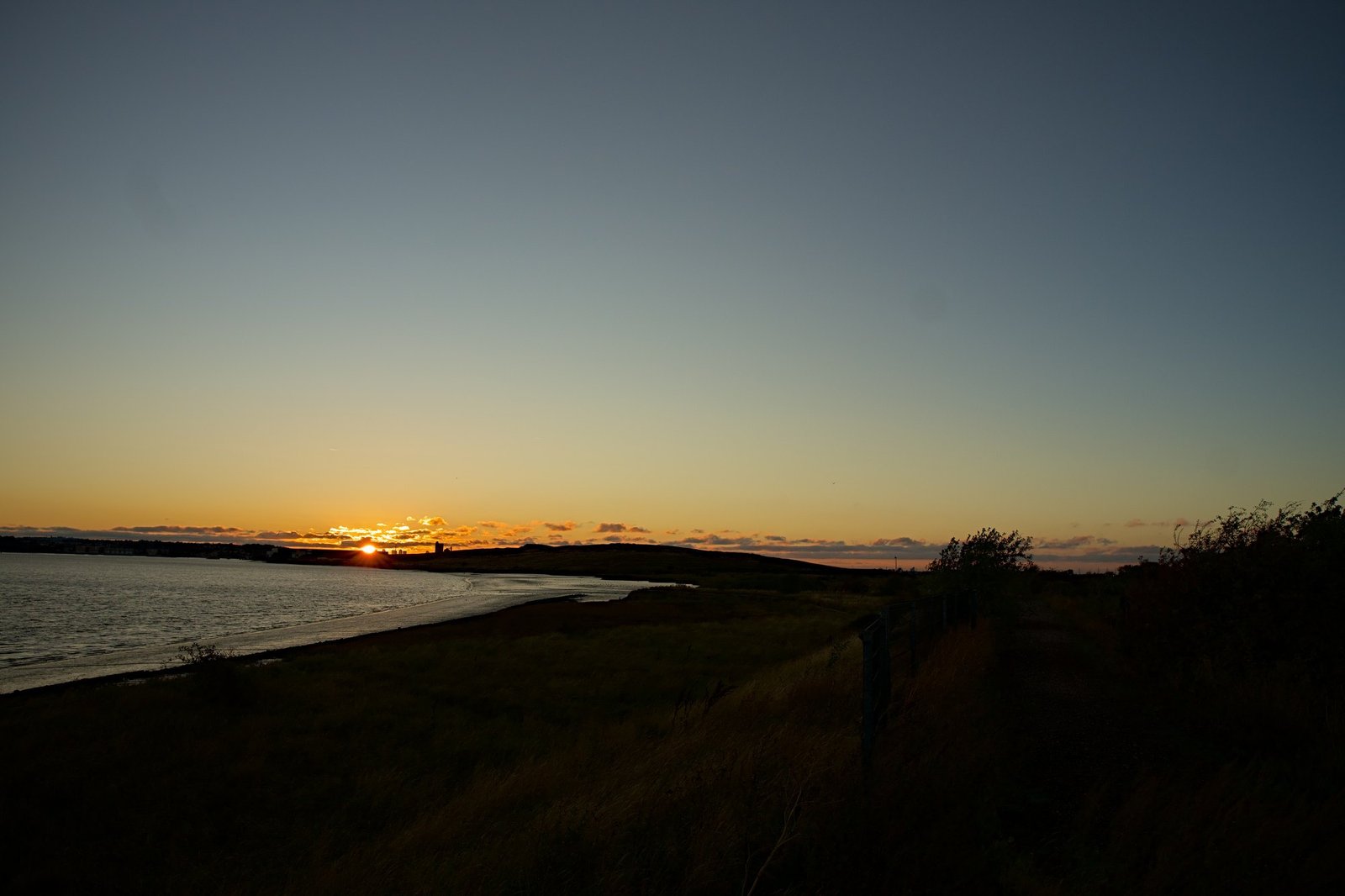The sun setting on the horizon over a curve of estuary shoreline