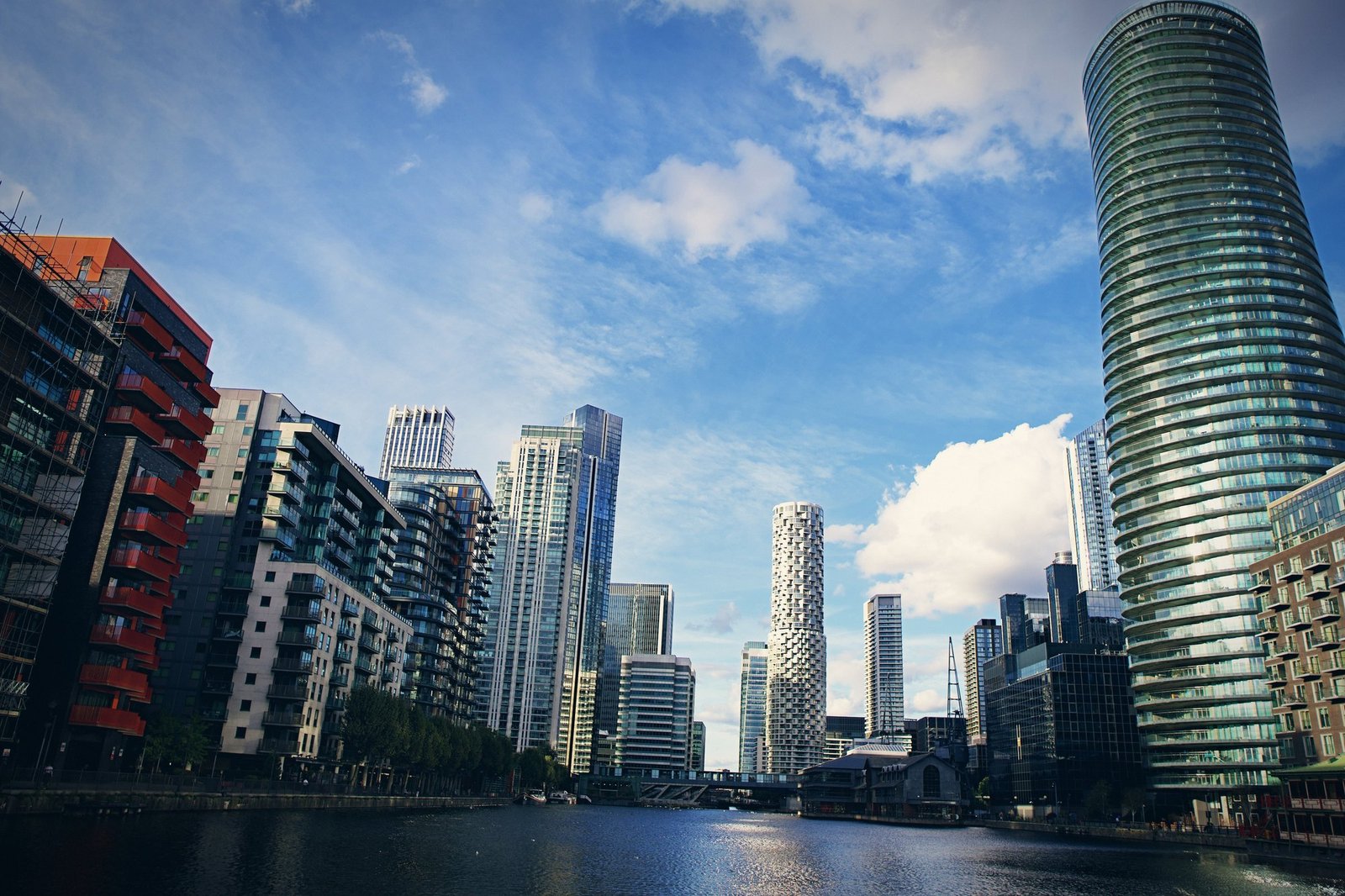 A wide view of Canary Wharf towers along the dock under broken cloud