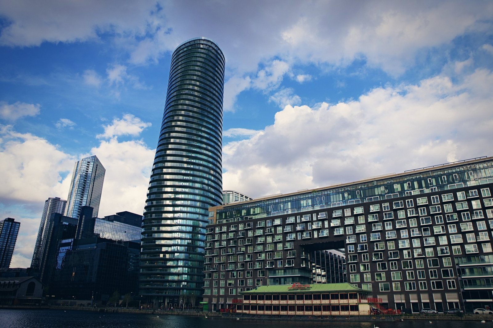 A curved glass residential tower beside a stepped brick block, clouds overhead