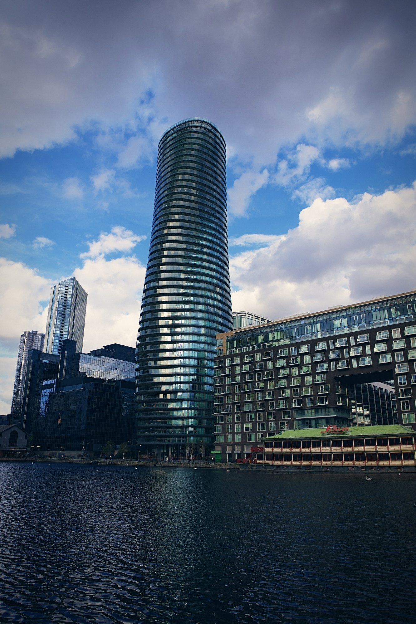 A tall curved glass tower rising over dock water, seen in portrait