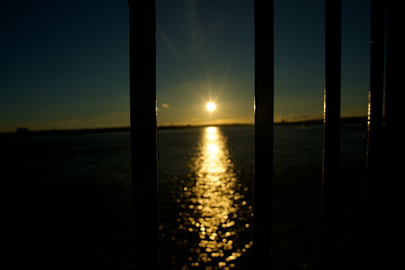 The setting sun and its reflection seen between dark vertical railing posts